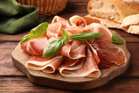 Slices of tasty cured ham and basil on wooden table, closeupの写真素材