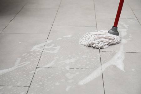Cleaning gray tiled floor with string mop, space for text