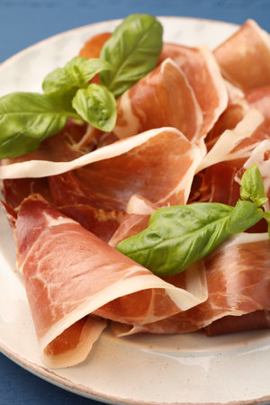 Slices of tasty cured ham and basil on plate, closeupの写真素材
