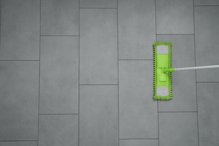 Cleaning gray tiled floor with microfiber mop, top view. Space for text