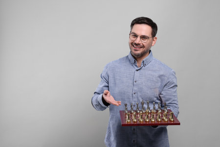 Smiling man showing chessboard with game pieces on light grey background, space for textの写真素材