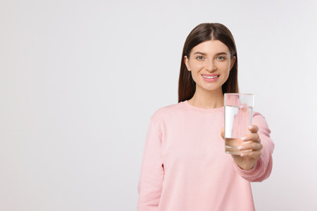 Healthy habit. Happy woman holding glass with fresh water on light gray background. Space for text