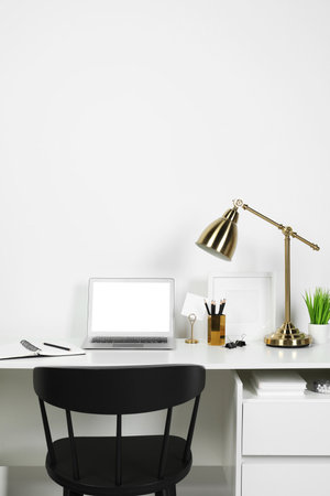Cozy workspace with laptop, lamp and stationery on wooden desk at homeの写真素材