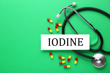 Card with the word Iodine, stethoscope and pills on green background, flat lay. Space for textの写真素材