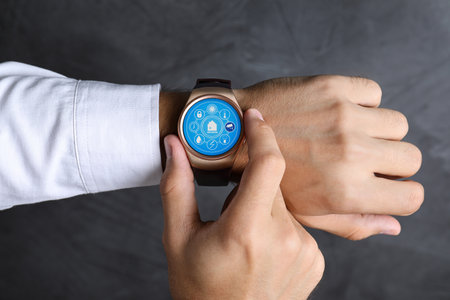 Man setting smart home control system via smartwatch against dark gray background, closeup. App...
