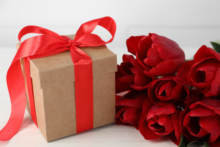 Beautiful gift box with bow and red tulip flowers on white table, closeupの写真素材