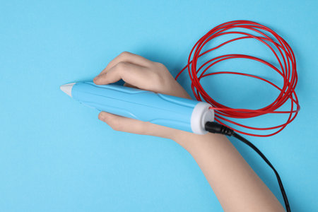 Boy drawing with stylish 3D pen on light blue background, top view