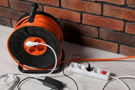 Extension cord reel on white floor near brick wall. Electrician's equipmentの写真素材