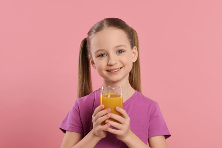 Cute little girl with glass of fresh juice on pink backgroundの写真素材