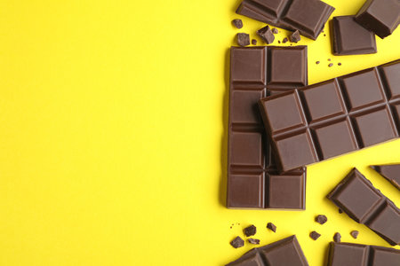 Pieces of delicious dark chocolate bars on yellow background, flat lay. Space for textの写真素材