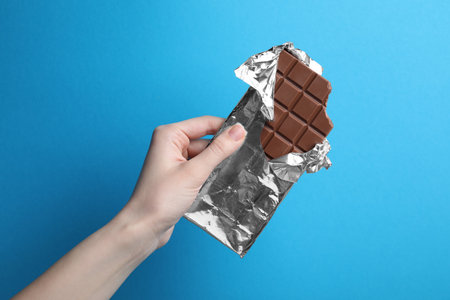 Woman holding delicious chocolate bar on light blue background, closeup