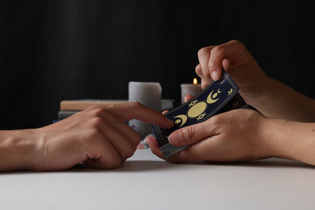 Astrologer predicting client's future with tarot cards at table, closeup