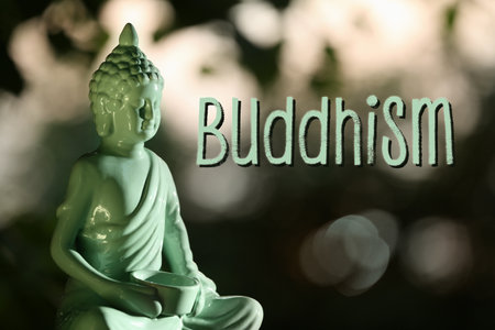 Decorative Buddha statue and word Buddhism on blurred background