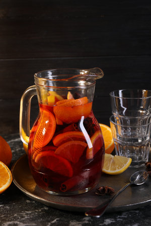 Jug of aromatic punch drink and ingredients on black tableの写真素材
