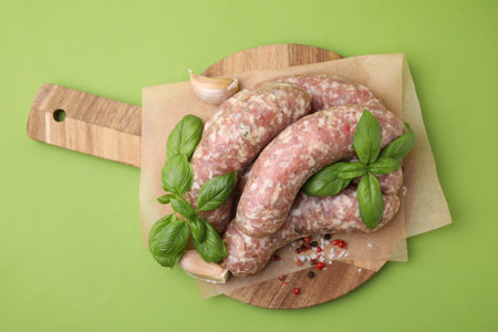Raw homemade sausages and different spices on green background, top viewの写真素材