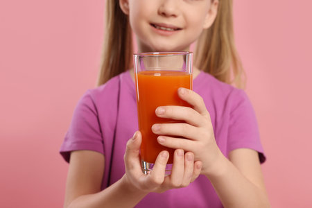 Cute little girl with glass of fresh juice on pink background, closeupの写真素材