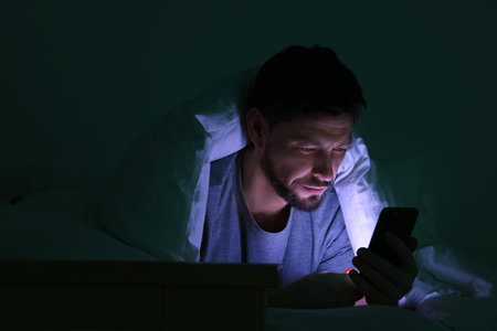 Man using smartphone under blanket in bed at night. Internet addictionの写真素材
