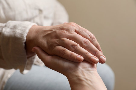 Woman holding hands with her mother on beige background, closeupの写真素材