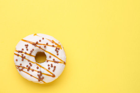 Tasty glazed donut decorated with sprinkles and caramel on yellow background, top view. Space for textの写真素材