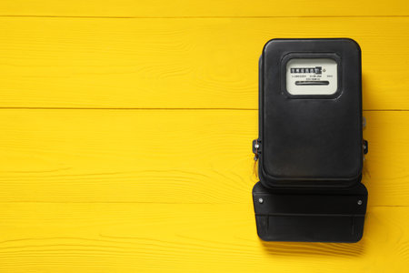Electricity meter on yellow wooden wall, space for text