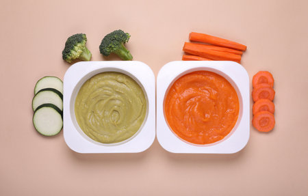 Bowls with healthy baby food and ingredients on beige background, flat layの写真素材