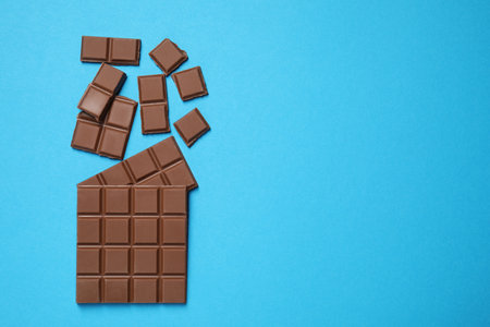Pieces of delicious chocolate bar on light blue background, flat lay. Space for text