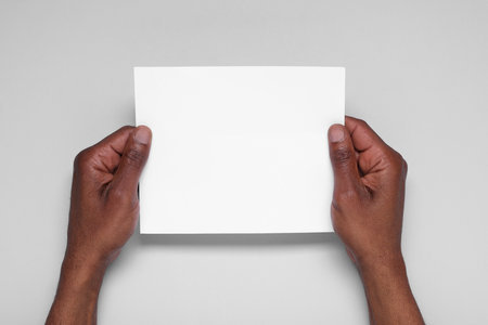 African American man holding sheet of paper on white background, closeup. Mockup for designの写真素材