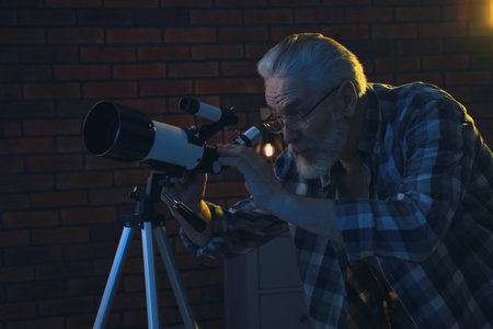 Senior man looking at stars through telescope in roomの写真素材