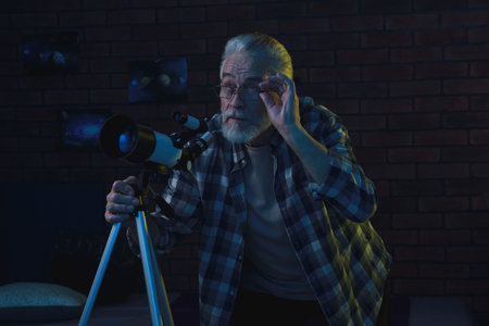 Senior man using telescope to look at stars in roomの写真素材