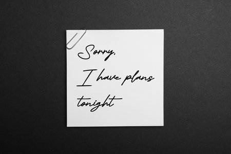 White note with phrase Sorry, I Have Plans Tonight on black background, top view