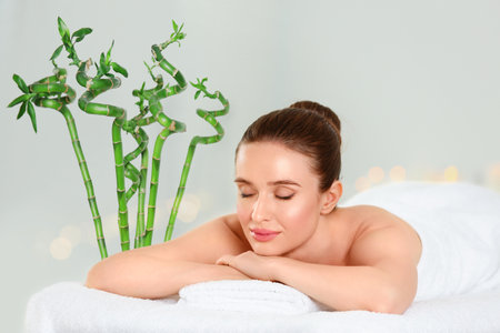Beautiful young woman relaxing in spa salon. Green bamboo stems on backgroundの写真素材