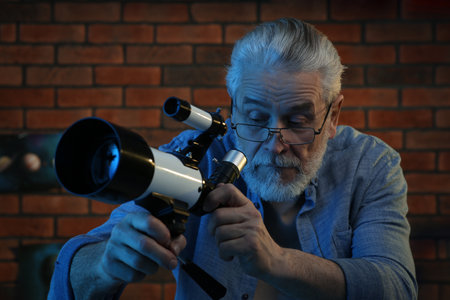 Senior man looking at stars through telescope in roomの写真素材