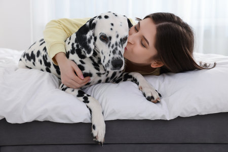 Beautiful woman kissing her adorable Dalmatian dog on bed at home. Lovely petの写真素材