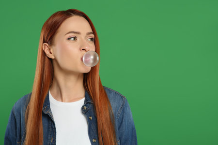 Beautiful woman blowing bubble gum on green background, space for textの写真素材