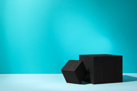 Black cubes on light table against turquoise background, space for text. Stylish presentation for productの写真素材