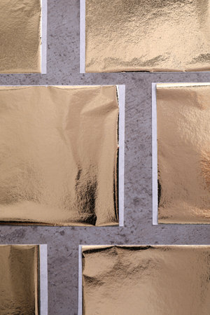 Many edible gold leaf sheets on gray textured table, flat lay