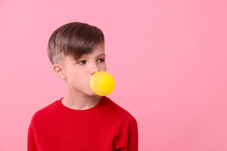 Boy blowing bubble gum on pink background, space for textの写真素材