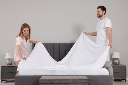 Couple changing bed linens in room. Domestic chores