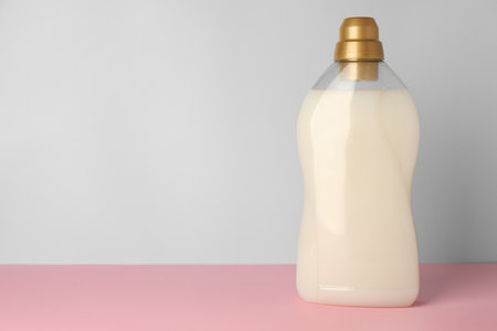 Bottle of fabric softener on pink table against light gray background, space for textの写真素材