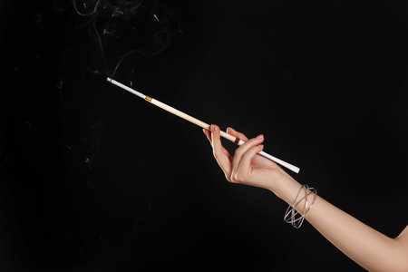 Woman holding long cigarette holder on black background, closeupの写真素材