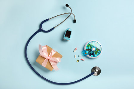 Stethoscope, pills, box and pulse oximeter on light blue background, flat lay. Medical giftの写真素材