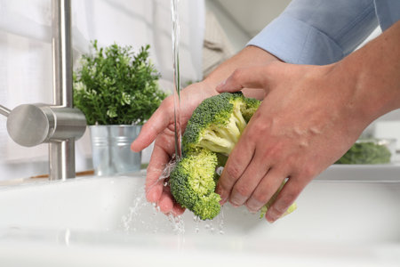 Man washing fresh broccoli in kitchen, closeupの写真素材