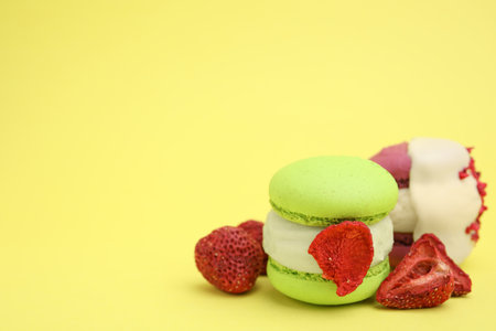 Delicious macarons and dry strawberries on yellow background, closeup. Space for textの写真素材