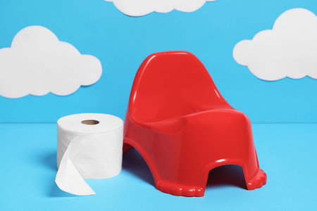 Red baby potty and bog roll against light blue background with paper clouds. Toilet trainingの写真素材
