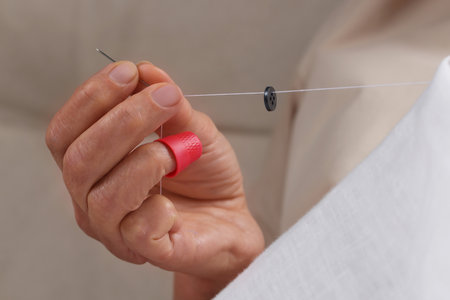 Woman sewing button with thimble and needle, closeupの写真素材