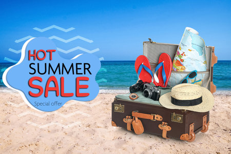 Hot summer sale flyer design. Suitcase with beach accessories on sand near sea and textの写真素材
