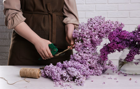 Woman trimming lilac branches with secateurs at white wooden table, closeupの写真素材