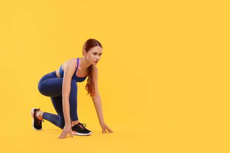 Young woman in sportswear getting ready to run on yellow background, space for text
