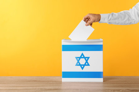 Man putting his vote into ballot box decorated with flag of Israel against yellow background, closeupの写真素材