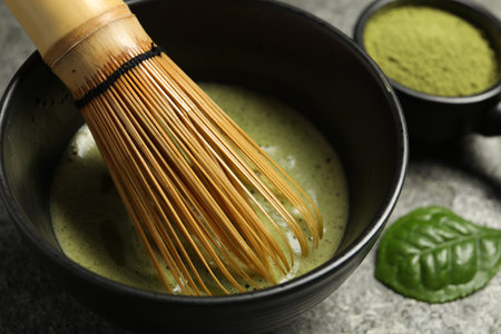 Cup of fresh green matcha tea with bamboo whiskey on gray table, closeup